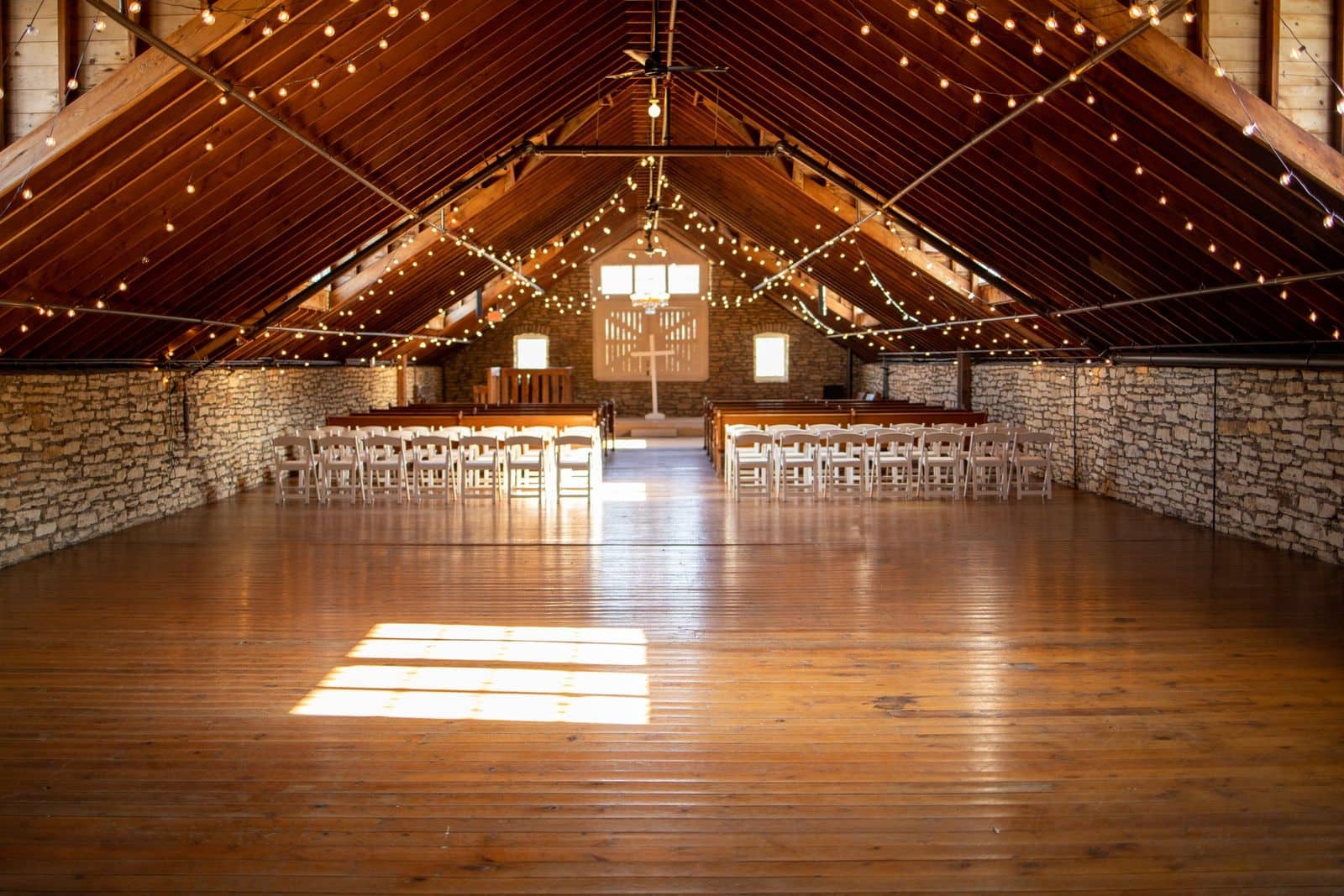 Long hardwood floor in a church hall with rows of chairs and pews